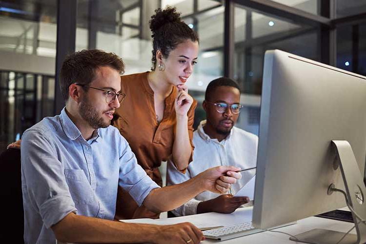 Image shows three people gathered around a computer screen together.